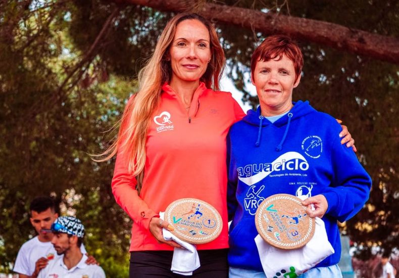 Two women proudly display awards at an outdoor sports event.